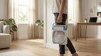 Person holding a portable fan in a room with light wood flooring and white walls.
