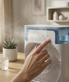 Hand adjusting a white and blue fan on a wooden surface with a blurred background